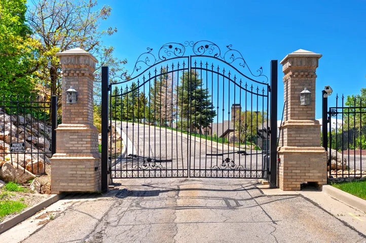 Wrought iron entry gates with scrollwork details, flanked by brick pillars with integrated lighting fixtures