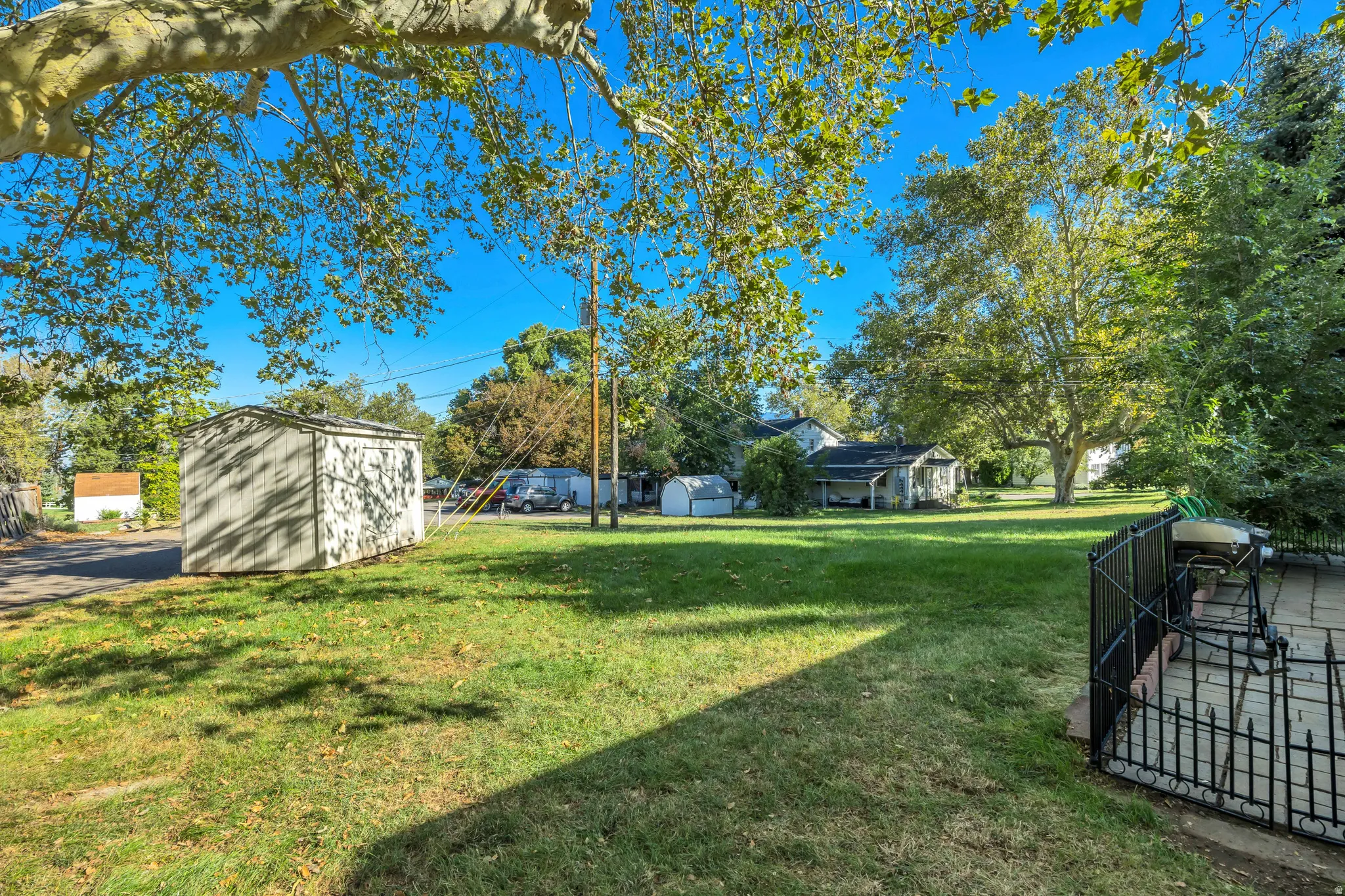 Expansive lawn with mature trees, detached storage shed, and paved patio area with black metal fencing