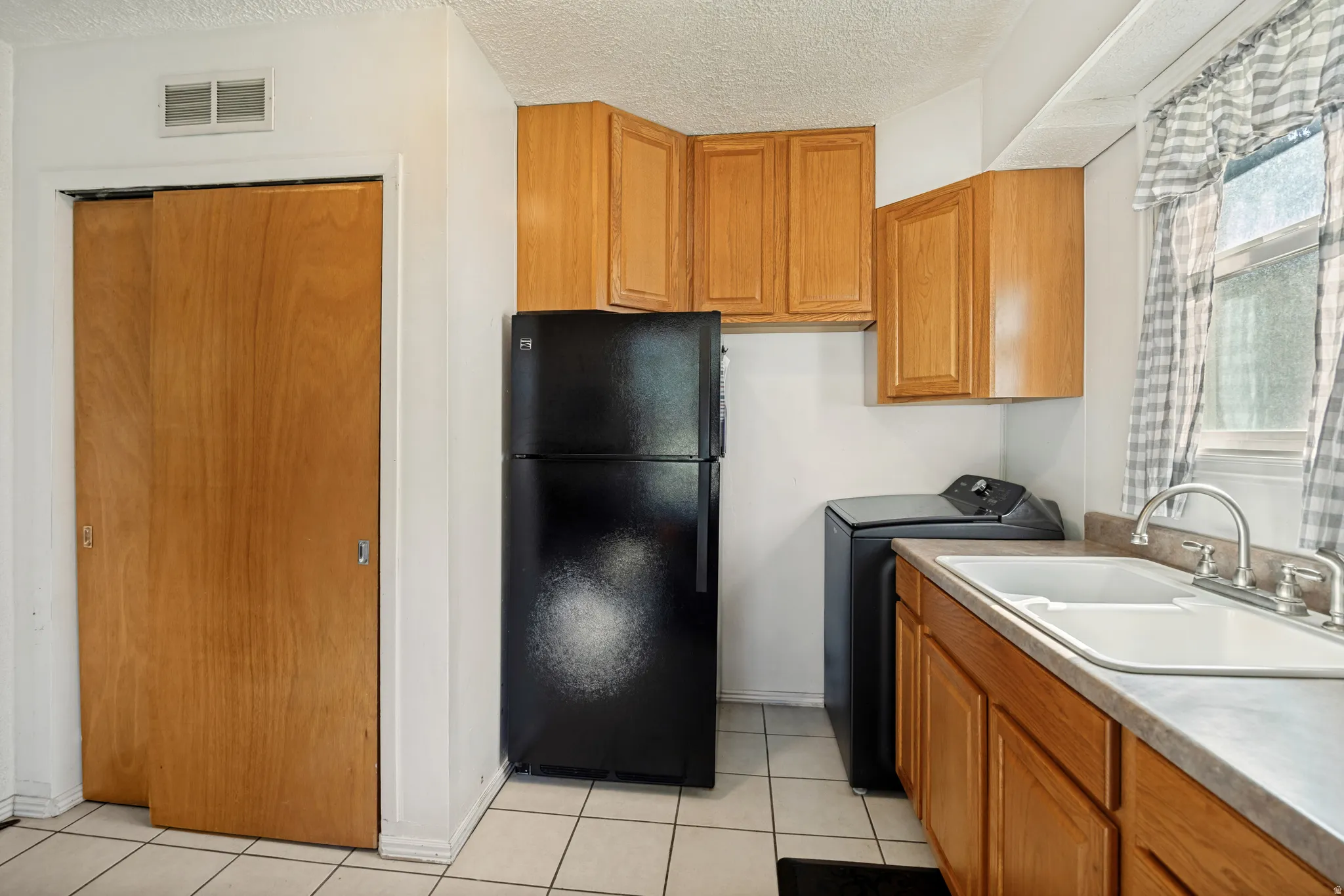 White tile flooring, wood-finish cabinetry, dual basin sink with chrome faucet, window with natural light, and sliding panel closet
