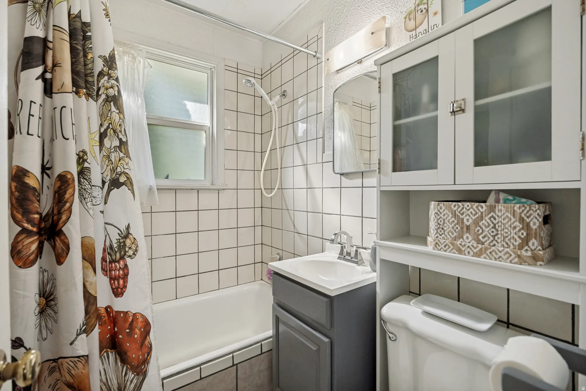White subway tile surround, built-in bathtub, vanity with integrated sink, wall-mounted medicine cabinet with frosted glass doors, and a toilet with an over-the-toilet storage unit