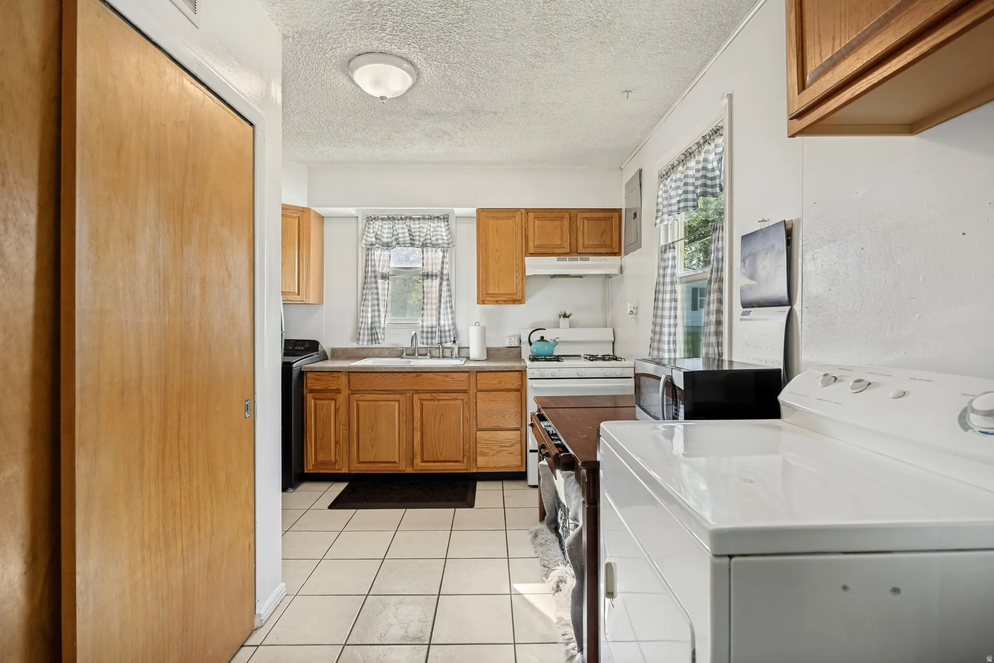Kitchen with wood-finish cabinetry, tile flooring, and integrated laundry appliances