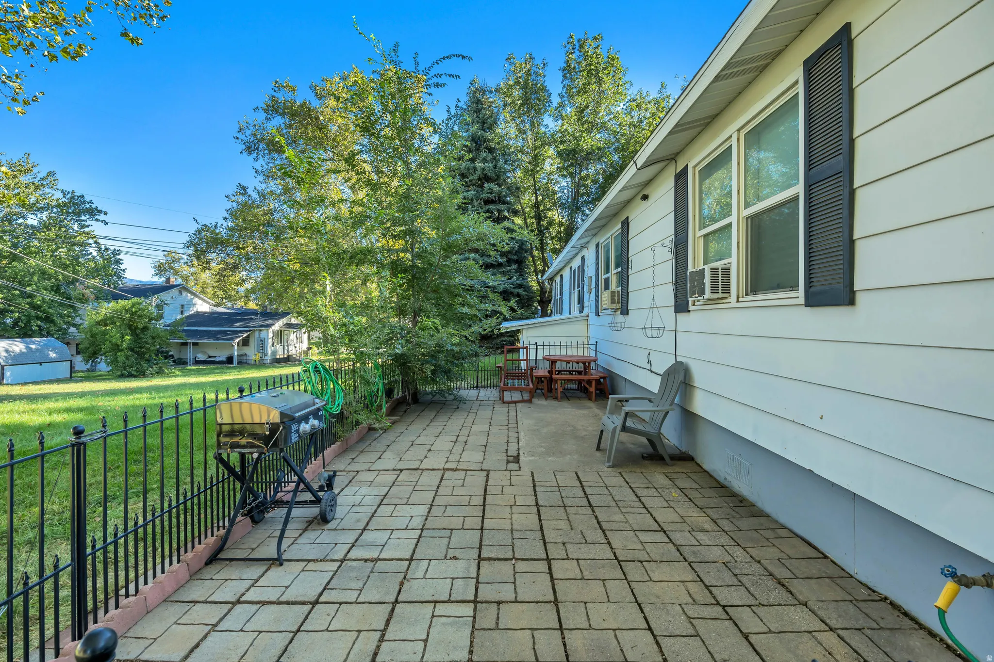 Paved patio area, white siding exterior, black window shutters, and a black wrought iron fence