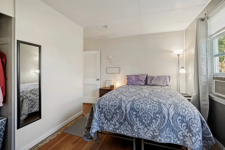 Hardwood flooring, painted interior walls, permanent window air conditioning unit, and a built-in closet with full-length mirror