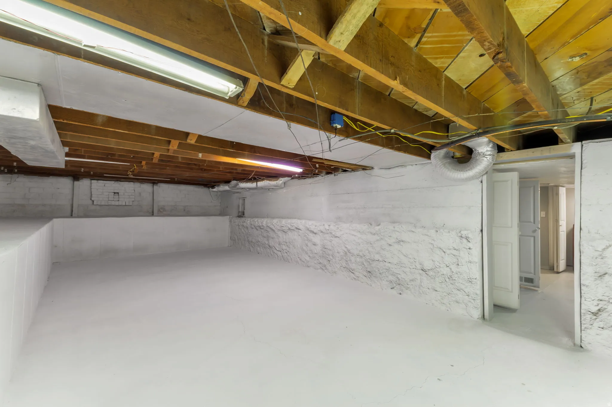 Exposed wooden ceiling beams, painted concrete walls, painted concrete flooring, fluorescent lighting, interior doors