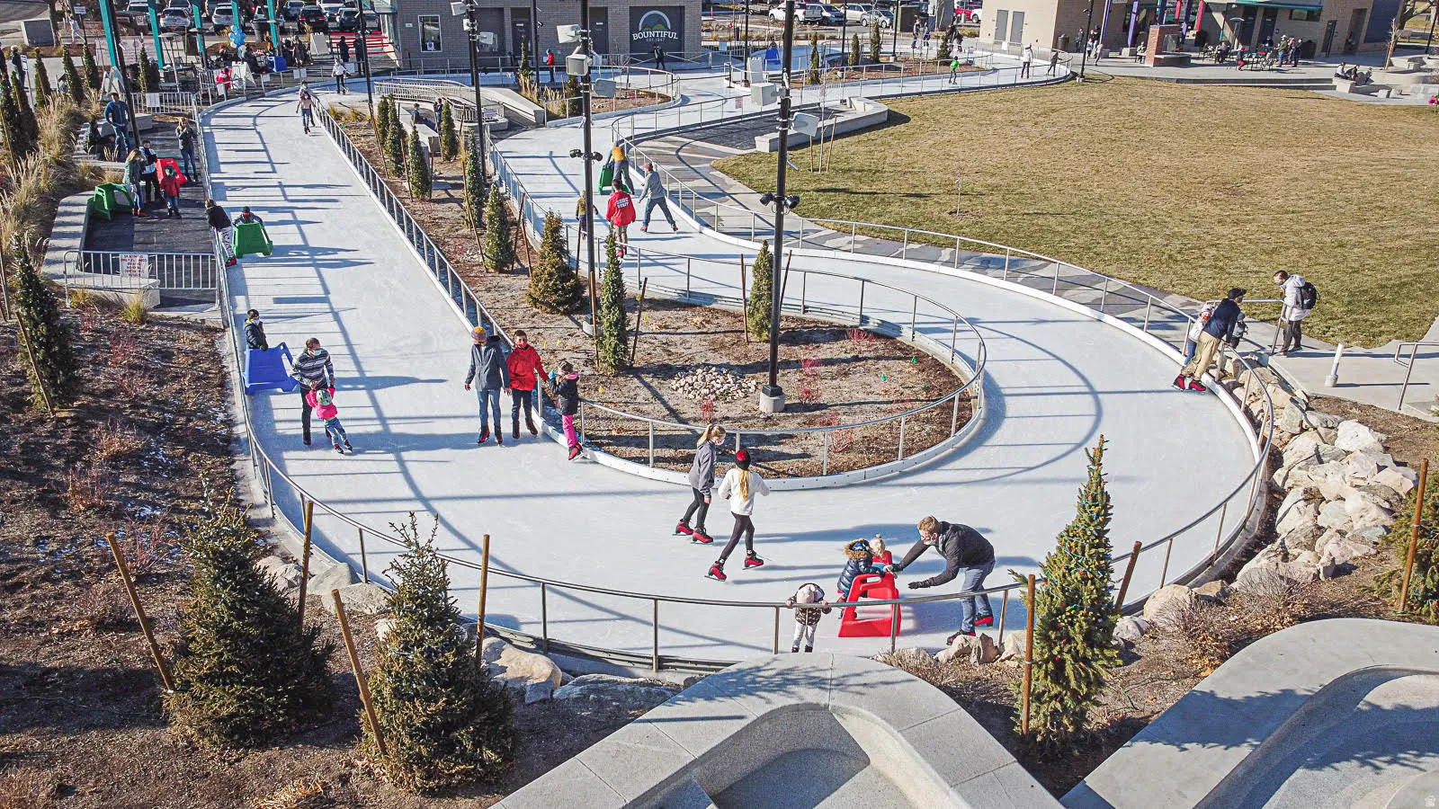 Expansive outdoor ice skating track with perimeter railings, surrounding landscaped areas, and a manicured lawn