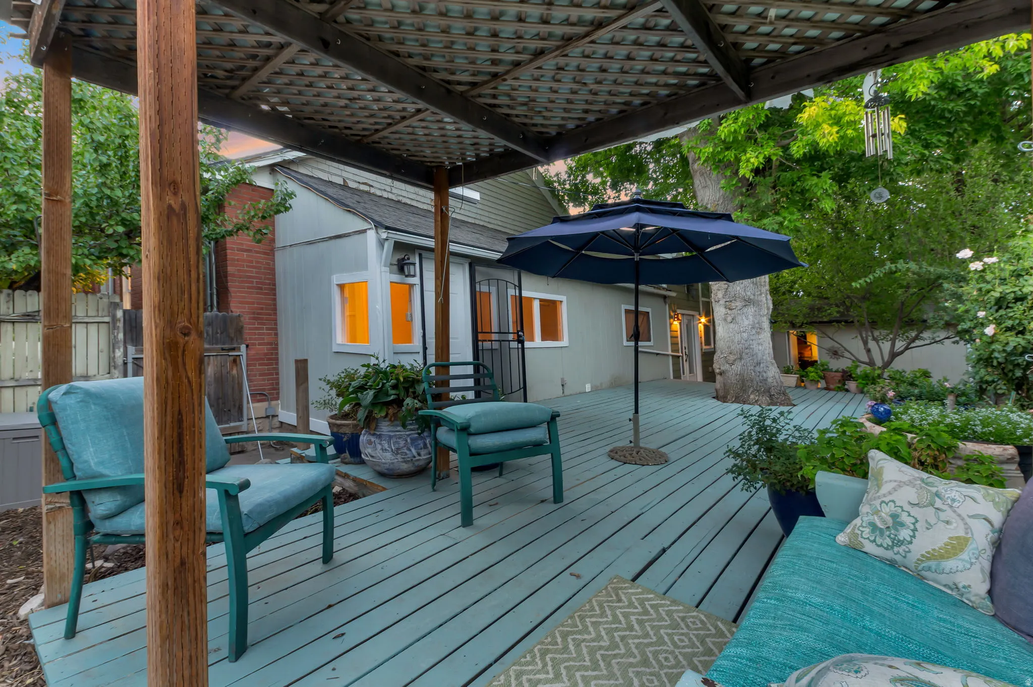 Expansive deck with a lattice pergola, mature landscaping, and exterior lighting