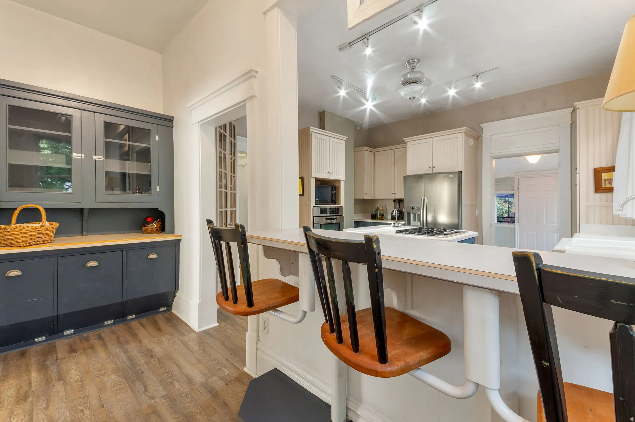 Kitchen featuring wood-finish flooring, built-in cabinetry with glass inserts, recessed lighting, and a stainless steel refrigerator