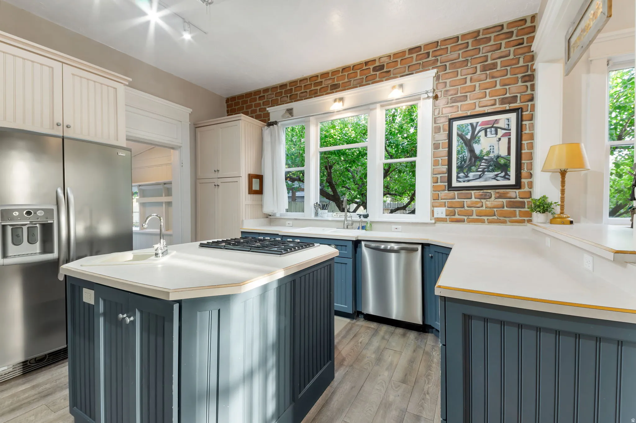 Kitchen with exposed brick wall, white countertops, stainless steel appliances, and a central island with an integrated cooktop and sink