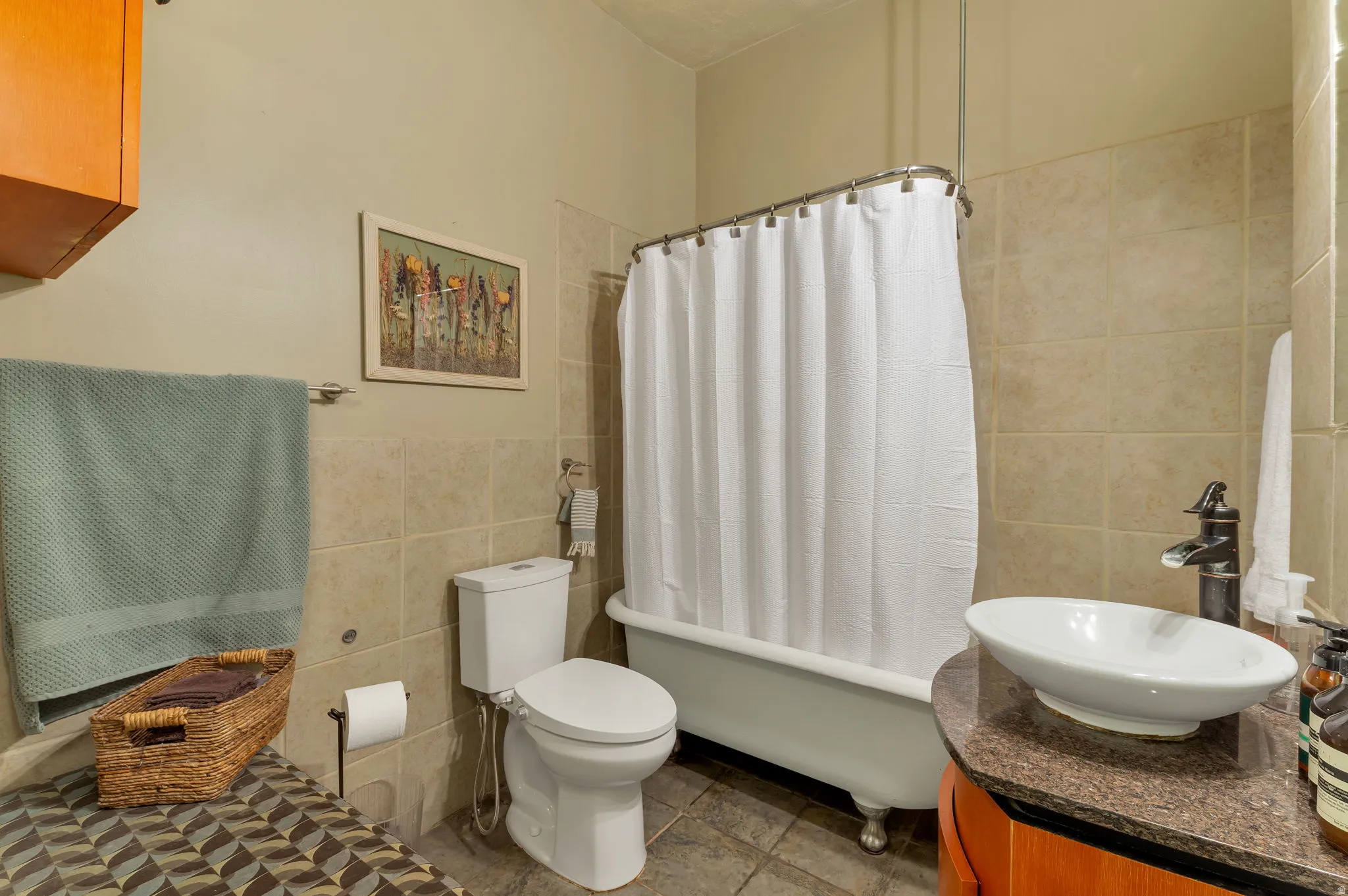 Clawfoot tub with shower, vessel sink, vanity with stone-look countertop, wood-finish cabinetry, and tiled walls