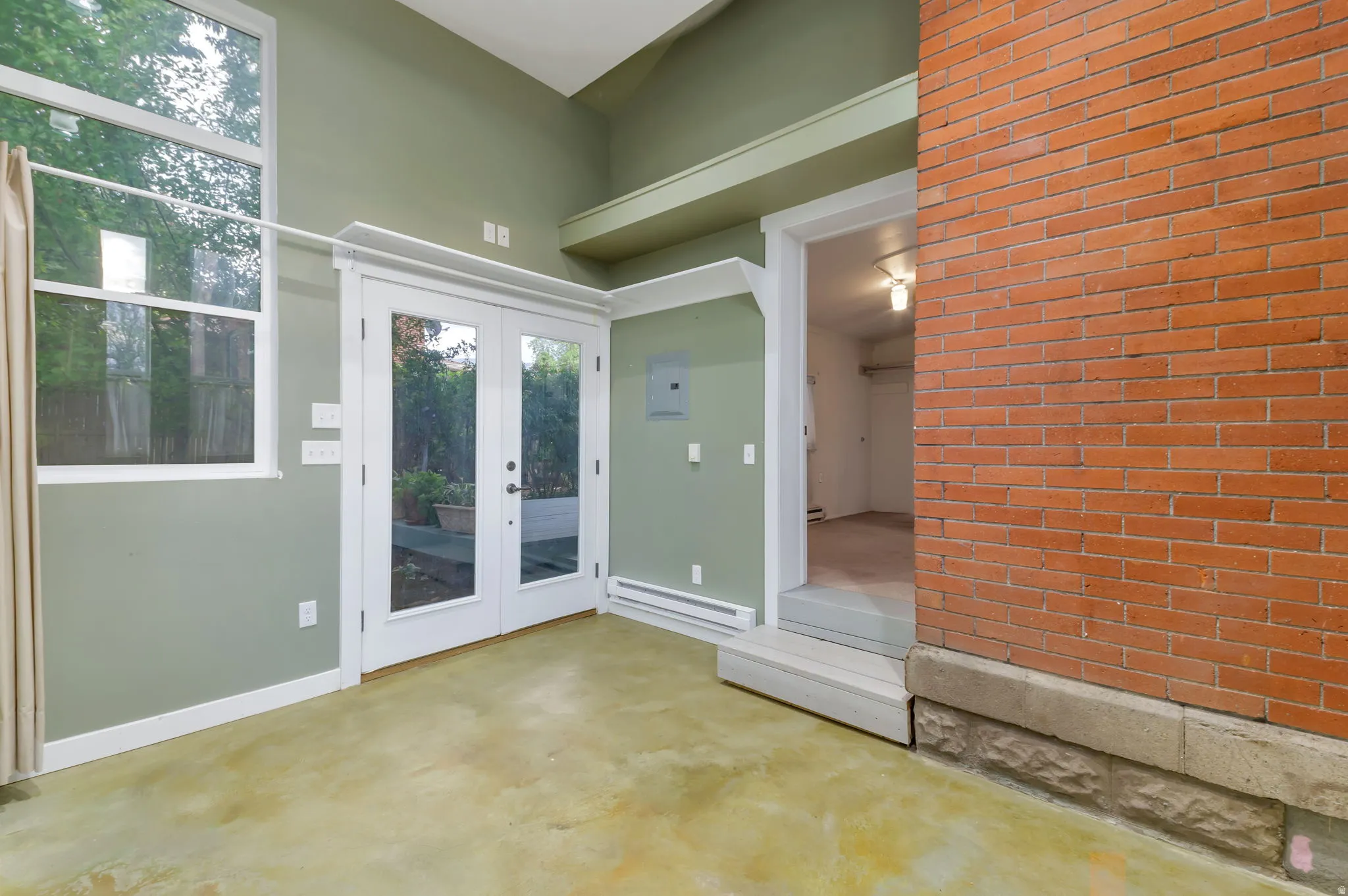 Concrete flooring, white-framed French doors, high windows, exposed brick wall, and built-in shelving