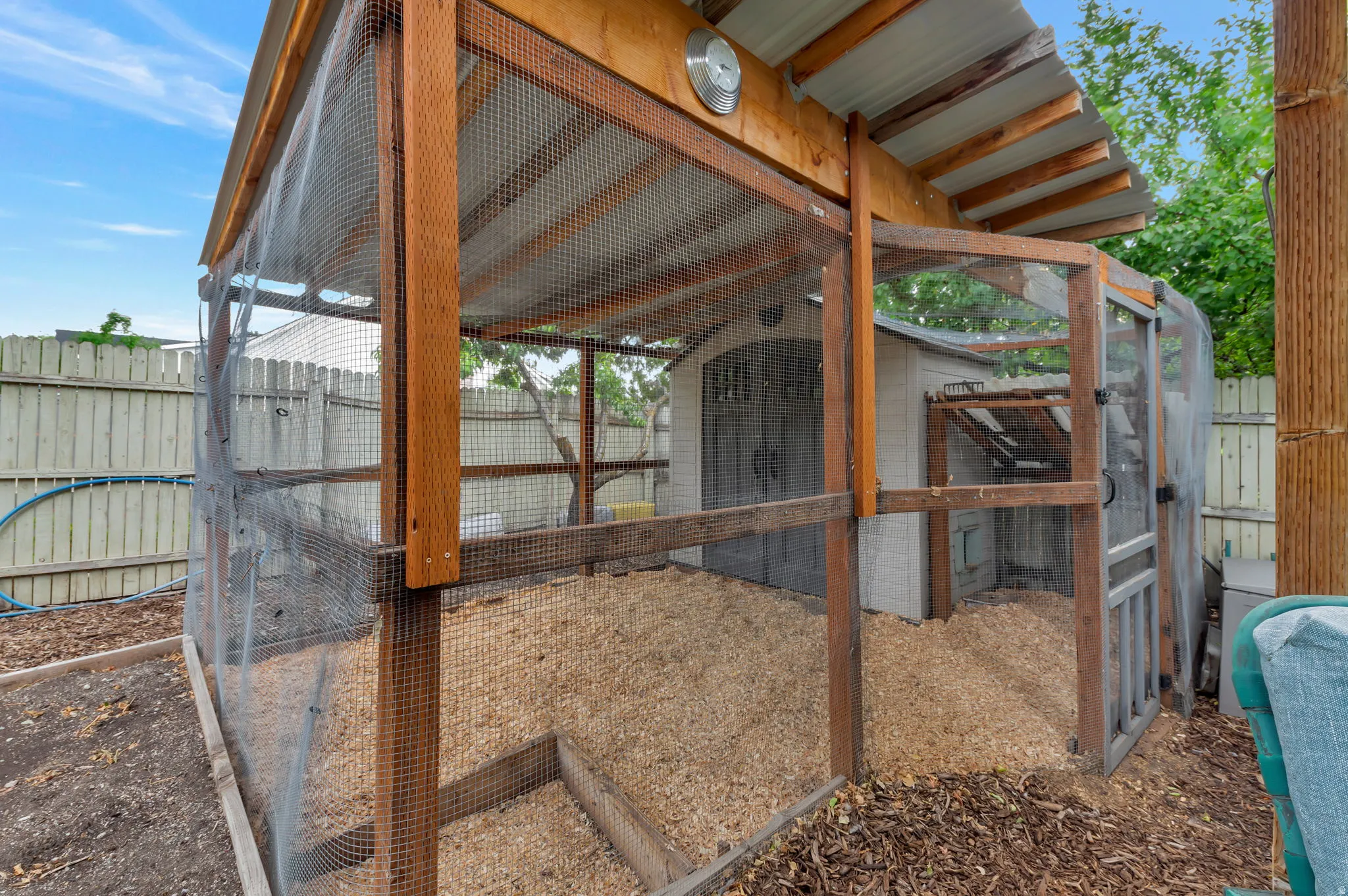 Enclosed outdoor structure with wood framing, metal roofing, wire mesh walls, and a separate integrated storage shed