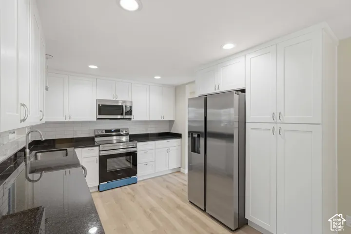 Kitchen featuring white shaker-style cabinetry, dark countertops, a stainless steel appliance suite, recessed lighting, and wood-finish flooring