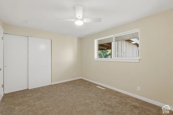 Neutral paint, plush carpet, white trim, sliding closet doors, and a ceiling fan with integrated lighting