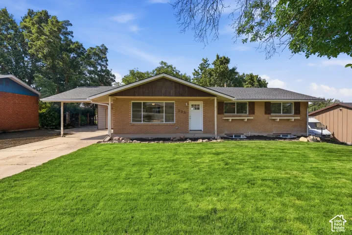 Brick exterior with dark wood trim, covered carport, front yard with green grass, and established trees