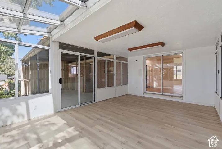 Sunroom featuring wood-finish flooring, glass paneled walls, and a glass roof
