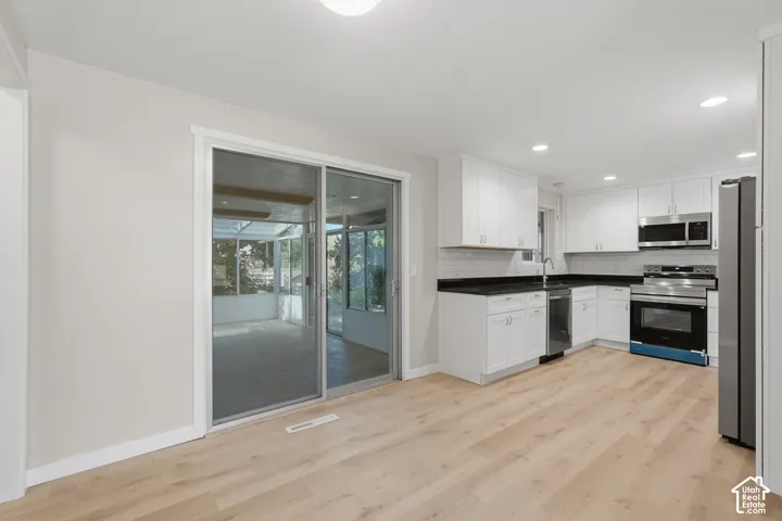 Modern kitchen featuring stainless steel appliances, white cabinetry, dark countertops, and wood-finish flooring