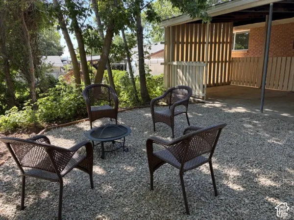 Gravel outdoor area with mature trees, a covered patio with wood slat privacy screening, and brick exterior accents