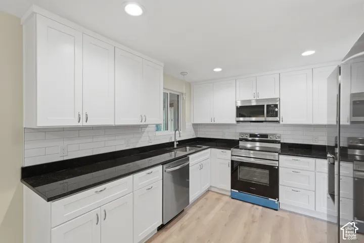 Well-appointed kitchen featuring white shaker cabinetry, dark countertops, a subway tile backsplash, recessed lighting, and stainless steel appliances