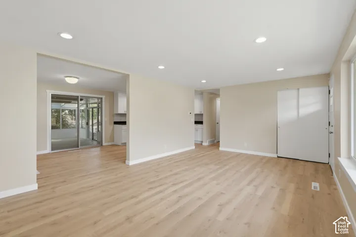 Recessed lighting, light wood-finish flooring, white trim, sliding glass doors, and a white entry door