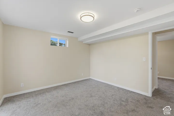 Spacious basement room featuring neutral wall finishes, plush carpeting, recessed ceiling lighting, and abundant natural light from high windows