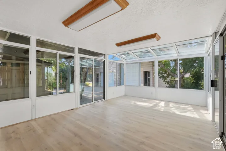 Expansive sunroom featuring a white frame, multiple windows, two sliding glass doors, a glass roof, and wood-finish flooring