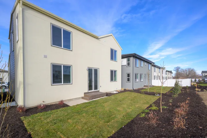 Rear exterior with a patio door, multiple windows, and a landscaped yard