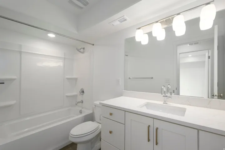 White vanity with brass hardware, undermount sink, and light-toned countertop