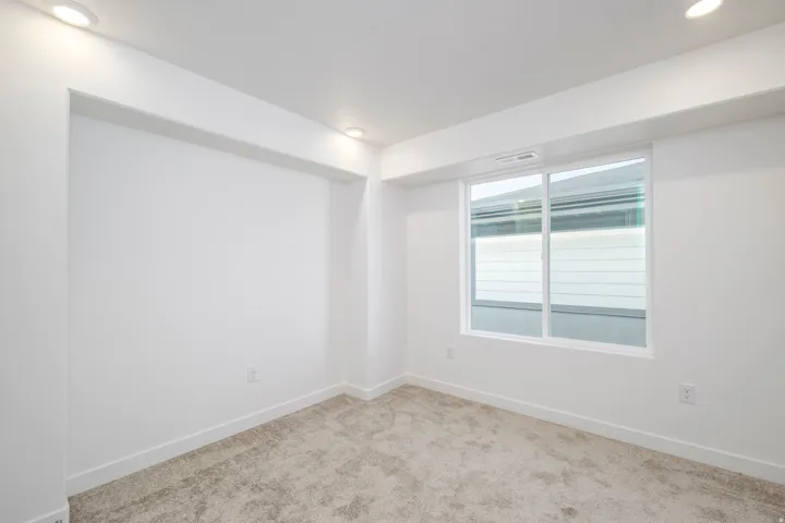 Recessed ceiling lighting, white walls, light-toned carpet, and a white-framed sliding window