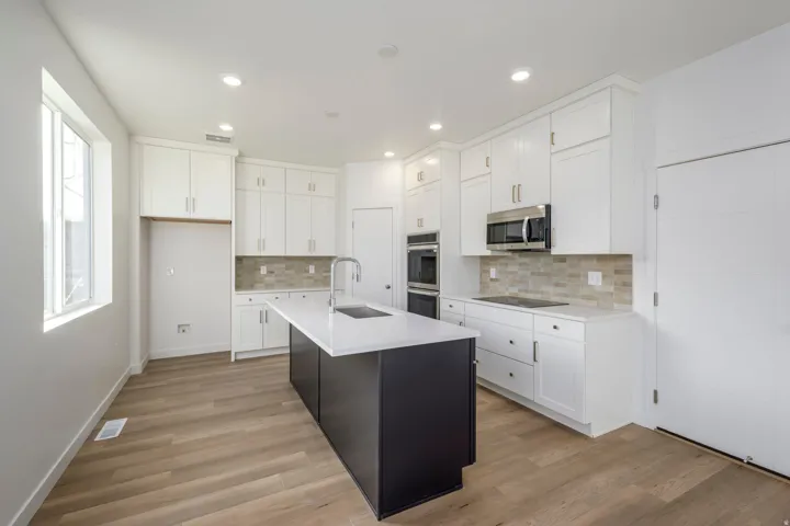 Kitchen featuring wood-finish flooring, white cabinetry, a dark-toned island with a white countertop and undermount sink, stainless steel appliances, and recessed lighting