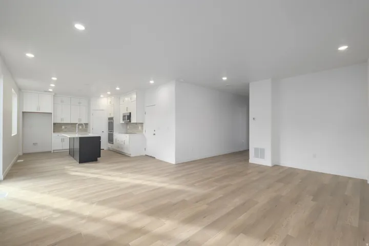 Open-concept living space with wood-finish flooring, recessed lighting, and a kitchen featuring white cabinetry, a dark-toned island, and built-in double ovens