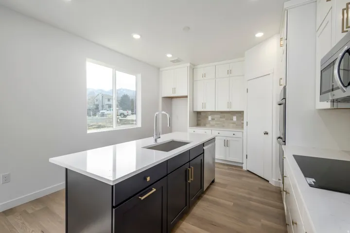 Modern kitchen featuring white cabinetry, a dark-toned island with a white countertop, stainless steel appliances, and wood-finish flooring