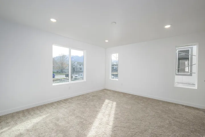 Recessed lighting illuminates a spacious room featuring carpeted flooring and multiple windows
