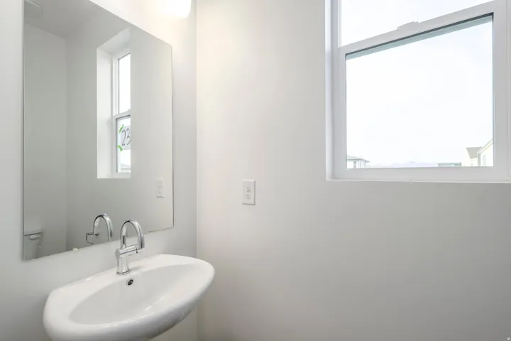 Wall-mounted basin sink with chrome faucet, large rectangular mirror, and a single window