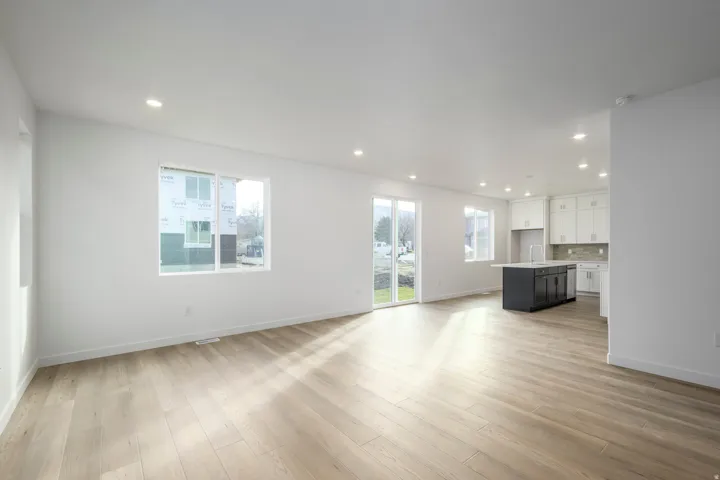 Recessed lighting, wood-finish flooring, white walls, white cabinetry, and a dark kitchen island with a sink
