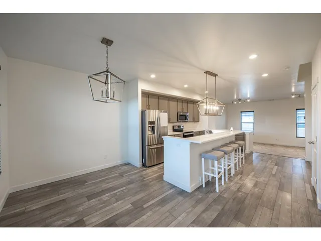 Open-concept living area featuring wood-finish flooring, recessed lighting, a kitchen island with seating, and stainless steel appliances