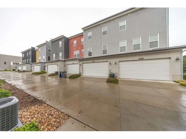 Multi-story stucco townhomes featuring attached garages, concrete driveways, and exterior lighting fixtures