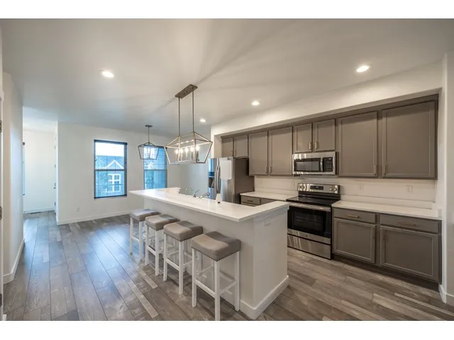 Modern kitchen featuring stainless steel appliances, grey cabinetry, white subway tile backsplash, quartz countertops.