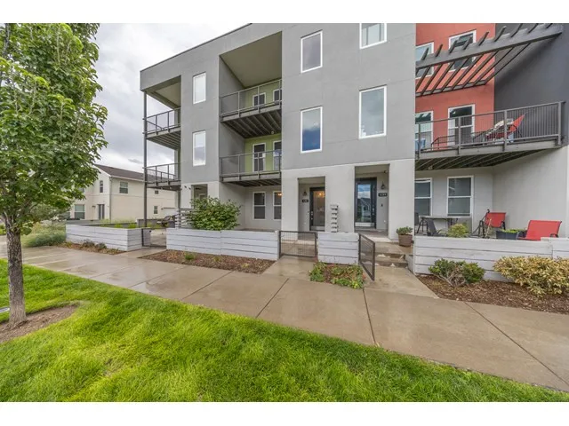 Modern multi-story building exterior with multiple balconies, a covered patio, and a concrete walkway
