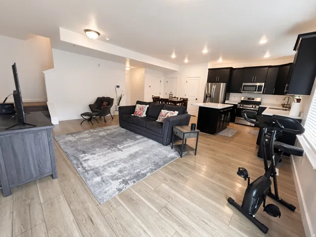 Open-concept living area with wood-finish flooring, recessed lighting, and a kitchen featuring dark cabinetry, stainless steel appliances, and a central island with a white countertop