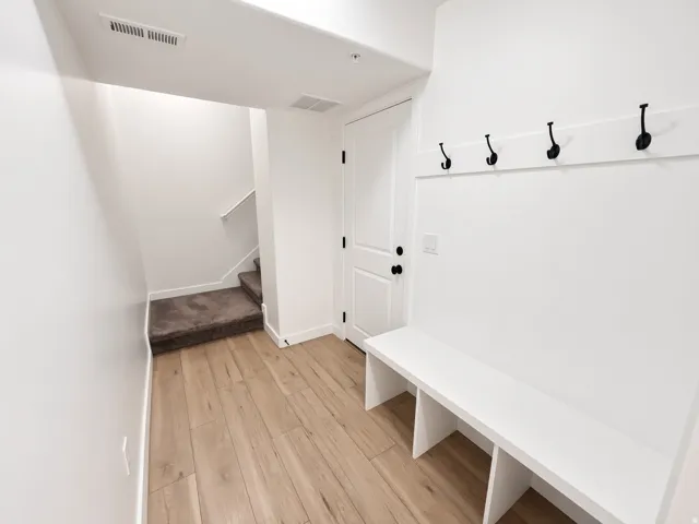 Wood-finish flooring, built-in storage bench, wall-mounted coat hooks, paneled interior door, and carpeted stairs