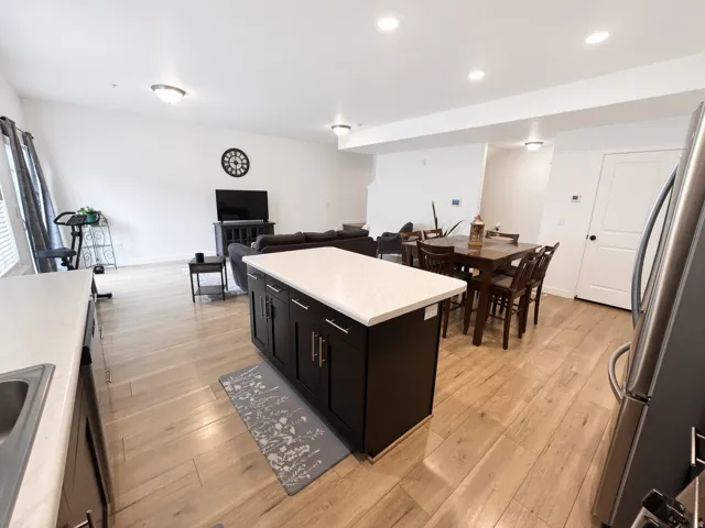 Open-concept living space with light wood-finish flooring, a kitchen island featuring dark cabinetry and a light-toned countertop, recessed lighting, and stainless steel appliances