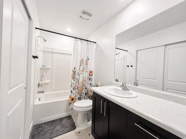 Bathroom featuring a built-in tub with shower, single vanity with integrated sink, dark wood-finish cabinetry, and a large wall-mounted mirror