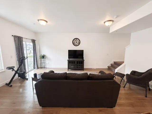 Expansive living area featuring light wood-finish flooring, recessed lighting, and a sliding glass door to an exterior balcony