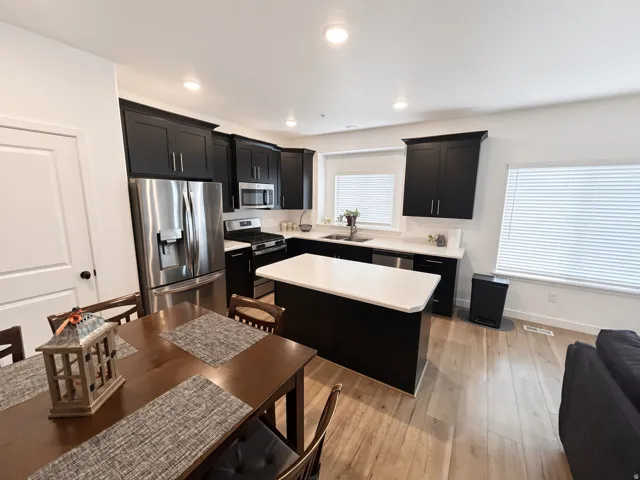 Kitchen featuring dark cabinetry, stainless steel appliances, a center island with a light-toned countertop, and wood-finish flooring