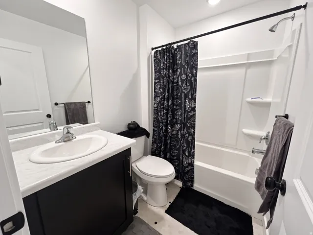 Bathroom featuring a vanity with an integrated sink, a full-width mirror, a toilet, and a combined tub and shower unit with built-in shelving
