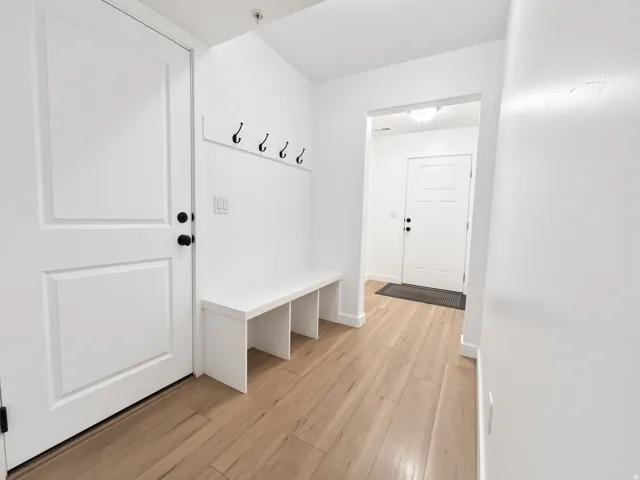 Light wood-finish flooring, white paneled doors with matte black hardware, built-in mudroom bench, and wall-mounted coat hooks