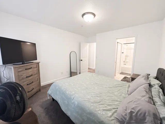 Carpeted room with white walls, a flush-mount ceiling light, and an en-suite bathroom featuring a white tub with shower