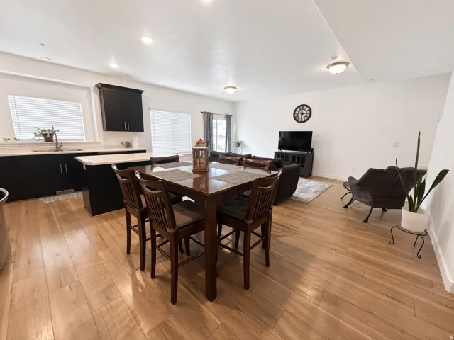 Open-concept living area featuring wood-finish flooring, white walls, recessed lighting, and a kitchen with dark cabinetry and light countertops