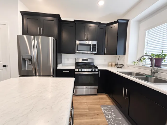 Kitchen featuring dark wood-finish cabinetry, stainless steel appliances, light-toned countertops, and wood-finish flooring