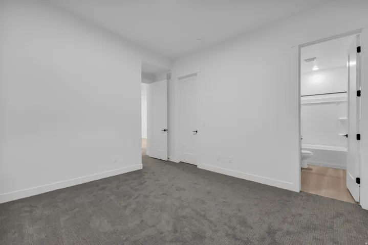 Neutral wall paint, gray carpet flooring, white trim, white doors with dark hardware, and a bathroom with a white bathtub and light-toned flooring